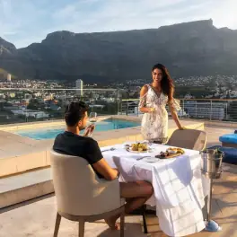 Couple dining on rooftop terrace by pool with mountain and city view