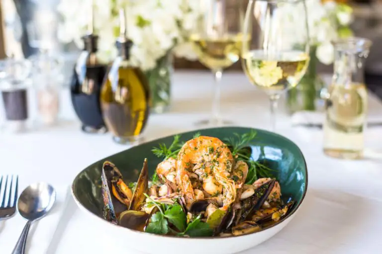 Seafood dish with shrimp, mussels and herbs beside wine glasses