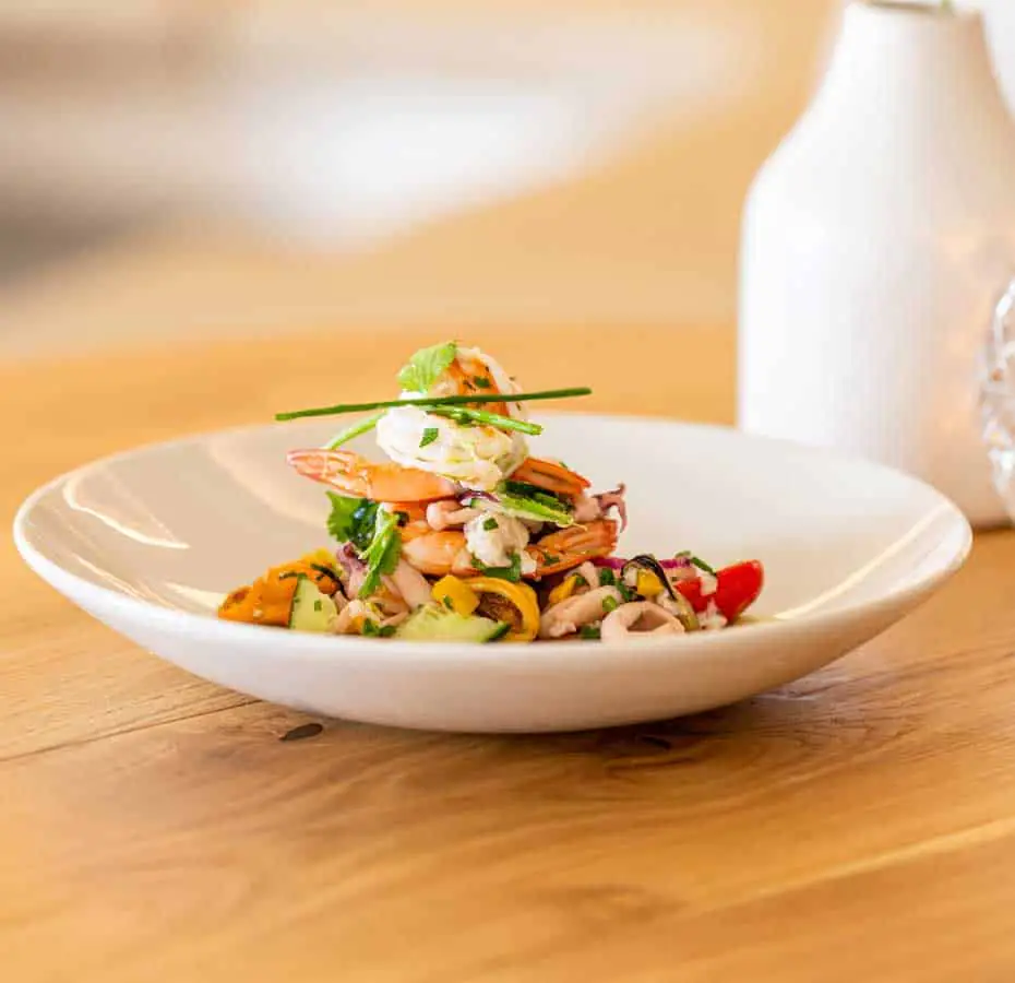 Shrimp and mixed seafood salad with grilled vegetables on white plate
