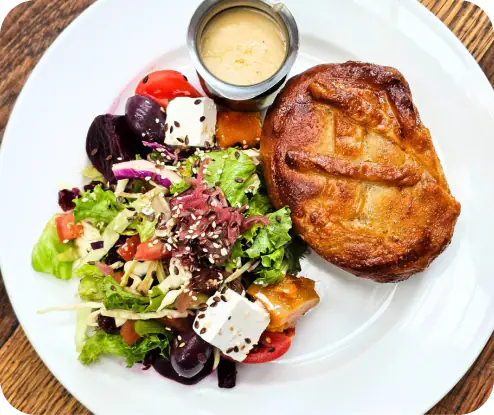 Savory pie with mixed salad, feta cubes, beets and dipping sauce on white plate