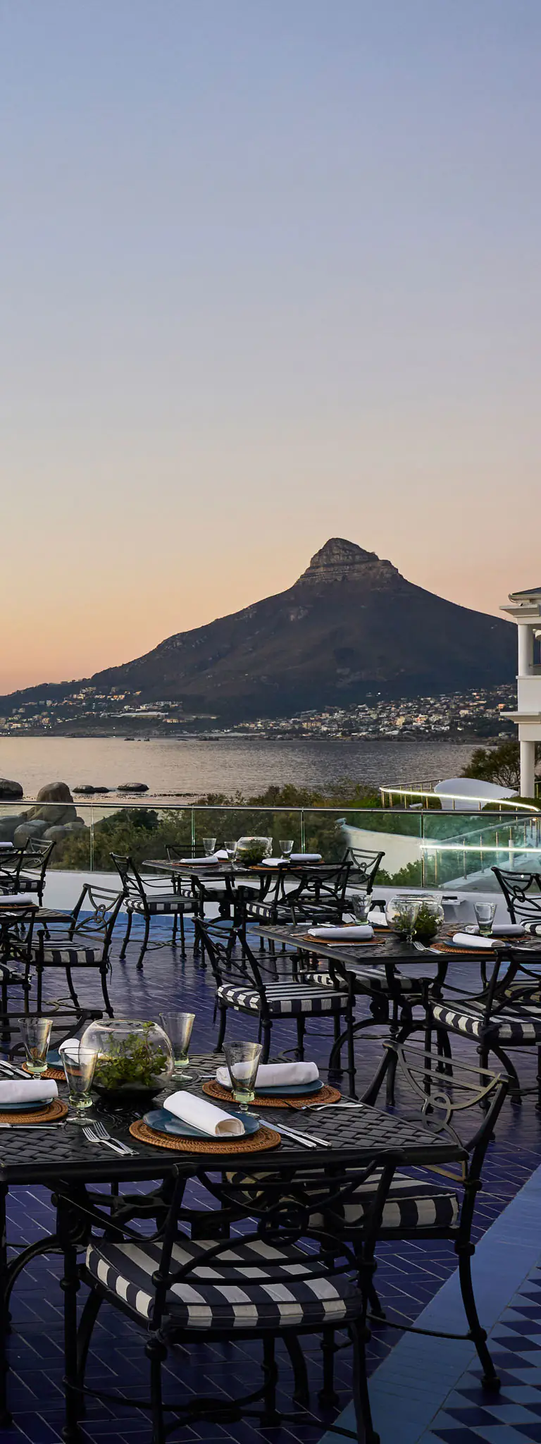 Outdoor terrace dining set overlooking sea and rocky mountain at sunset
