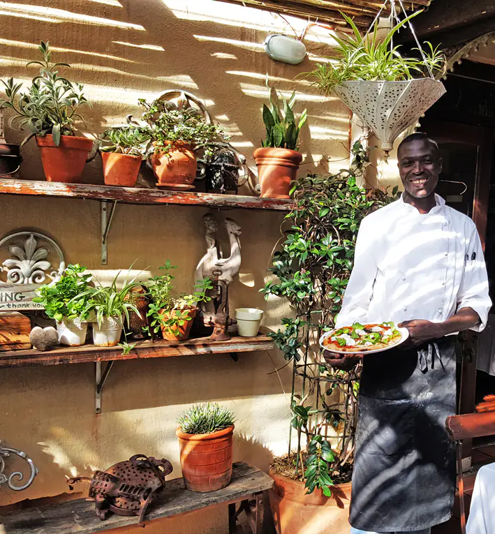 Smiling chef in outdoor plant-filled patio holding a plated salad