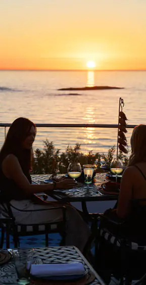 Two women dining on a seaside terrace at sunset