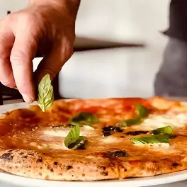 Hand placing fresh basil on Margherita pizza