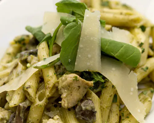 Penne pasta with pesto, chicken, arugula, and shaved Parmesan