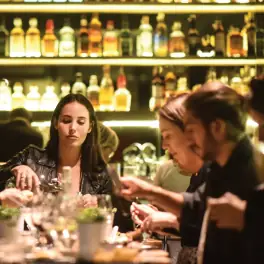Friends sharing a meal at a dimly lit bar with bottles behind