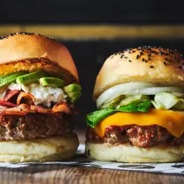 Two gourmet cheeseburgers with avocado, onions, and seeded buns