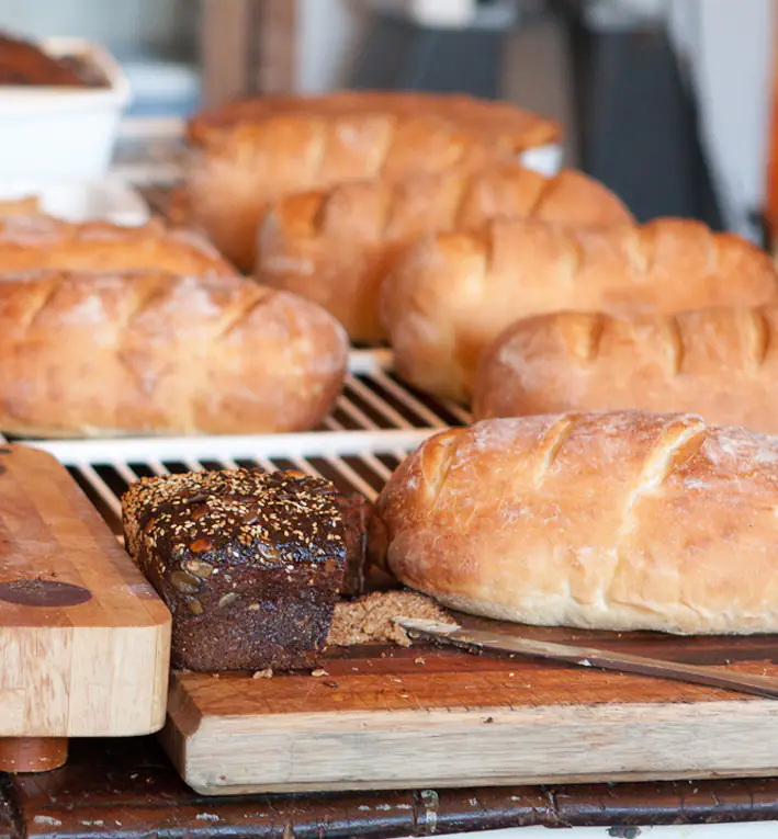 Assorted fresh loaves, including a seeded dark loaf, on cutting boards and a cooling rack
