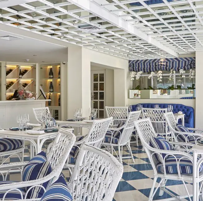 Coastal-style restaurant dining room with white wicker chairs and blue-striped cushions