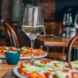 Glass of white wine on a restaurant table with pizza plates