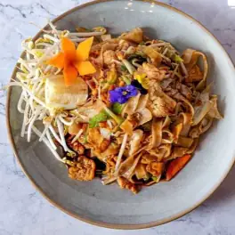 Stir-fried rice noodles with bean sprouts, crushed peanuts, herbs and edible flowers